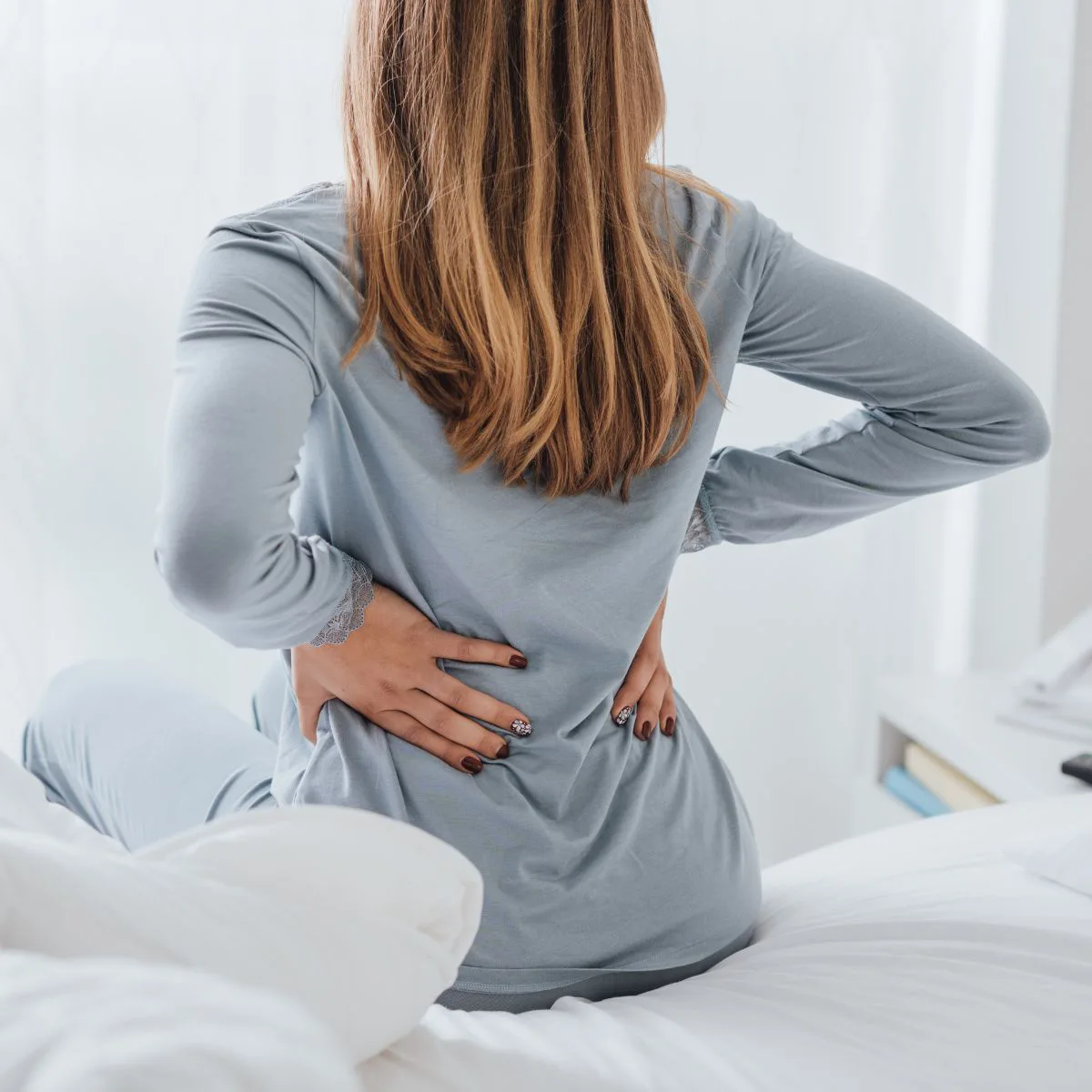 Woman sitting on bed holding her lower back in pain
