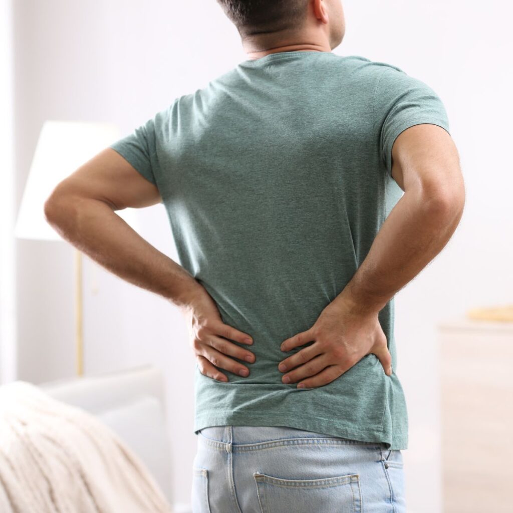 Man in a green shirt holding his lower back in discomfort