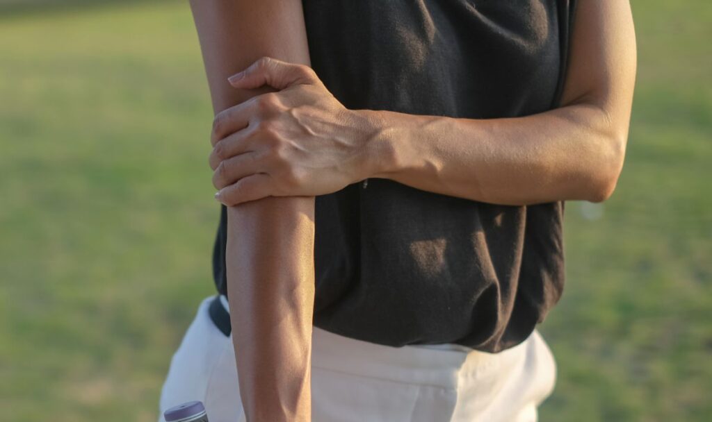 Person holding their forearm outdoors with one hand