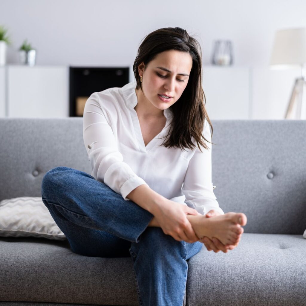 Woman sitting on a couch holding her foot in discomfort