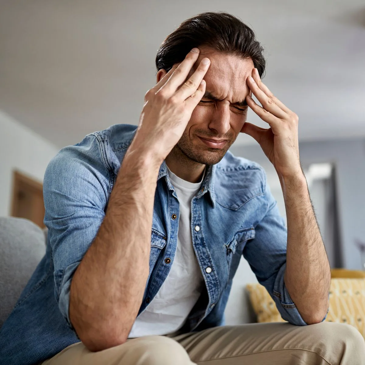 Man sitting on couch holding his head in pain from a headache