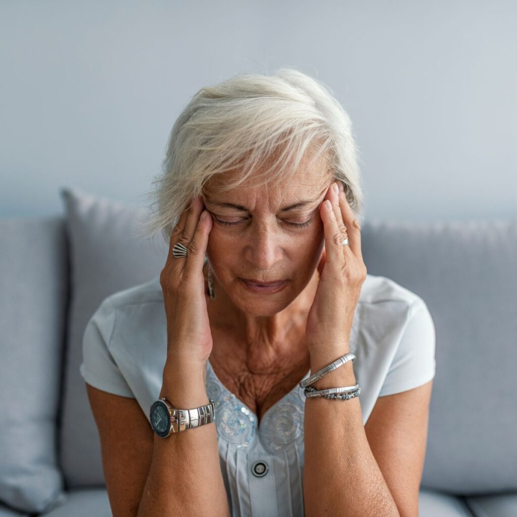 Elderly woman sitting with eyes closed and holding her temples in pain