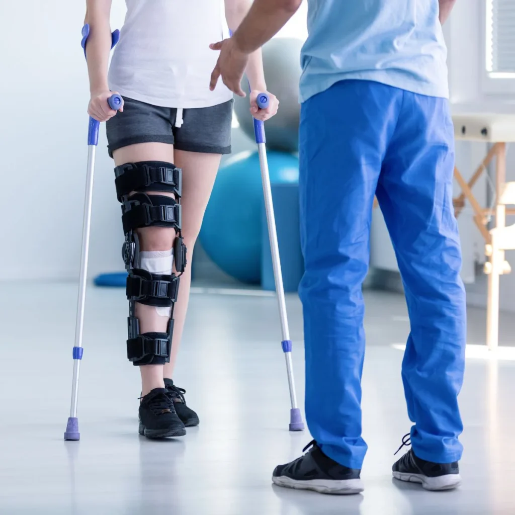 Patient with knee brace walking on crutches under supervision