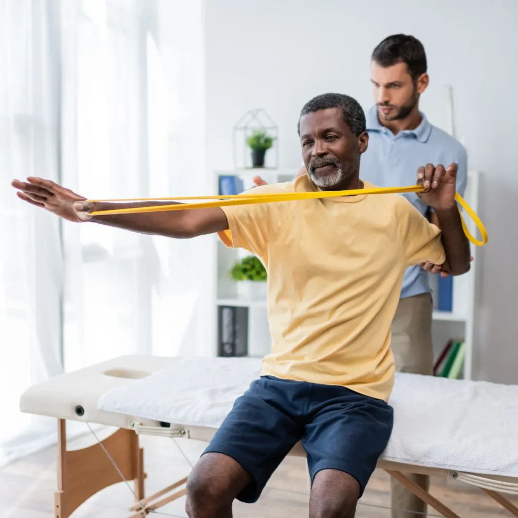 Older man doing resistance band shoulder exercises with therapist guidance