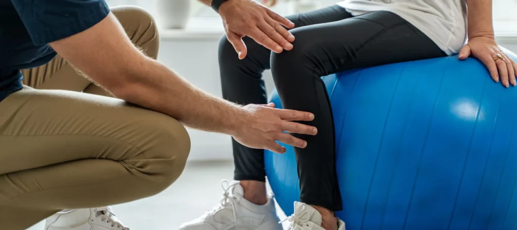 Therapist guiding a patient’s knee while seated on a blue exercise ball