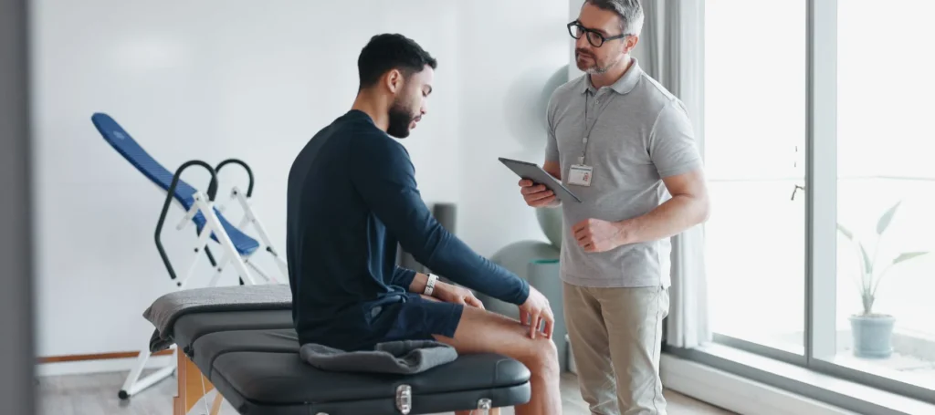 Therapist discussing treatment with a patient sitting on a table holding his knee